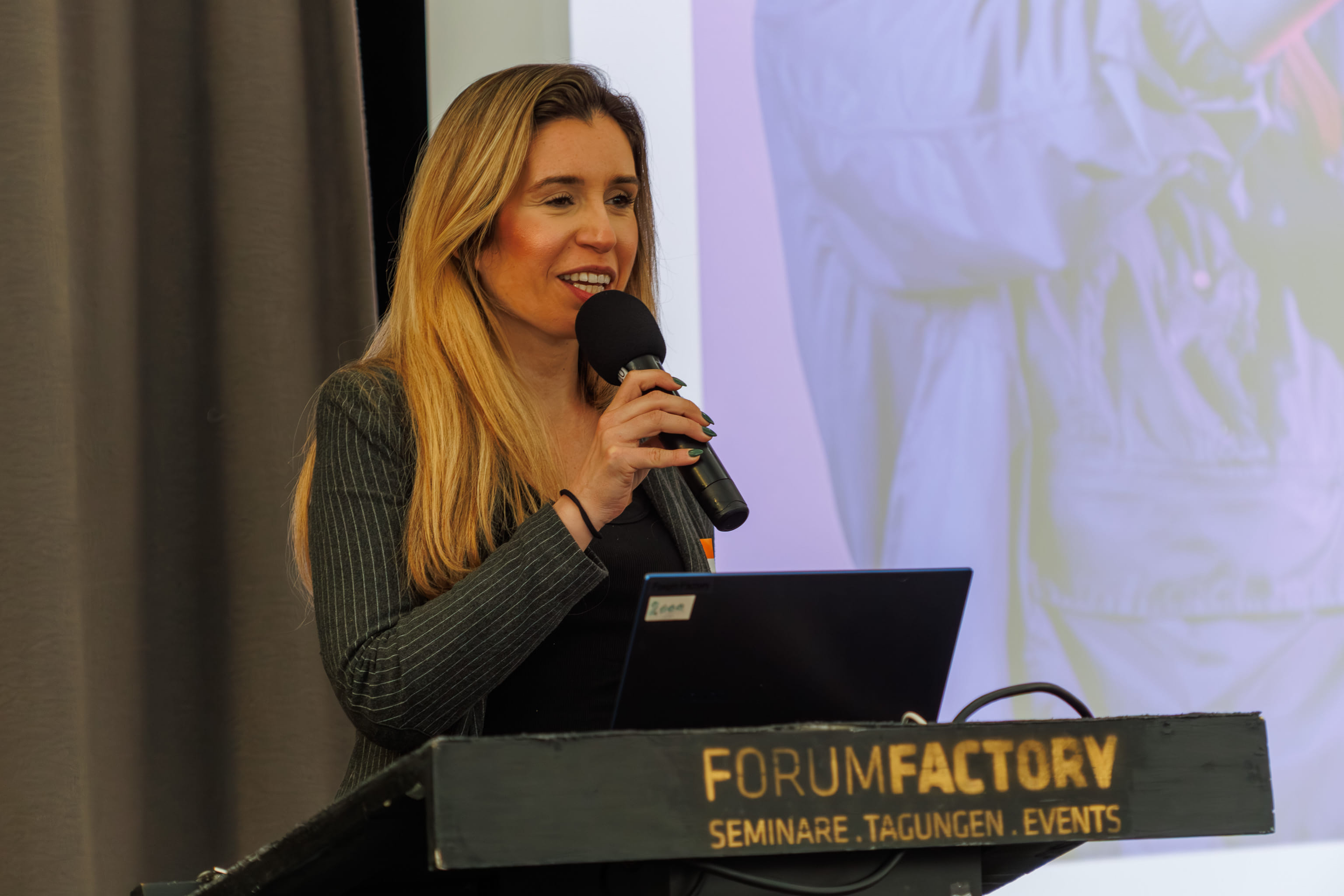 A speaker presenting on stage at XR Futures Conference 2026, FORUM Factory Berlin